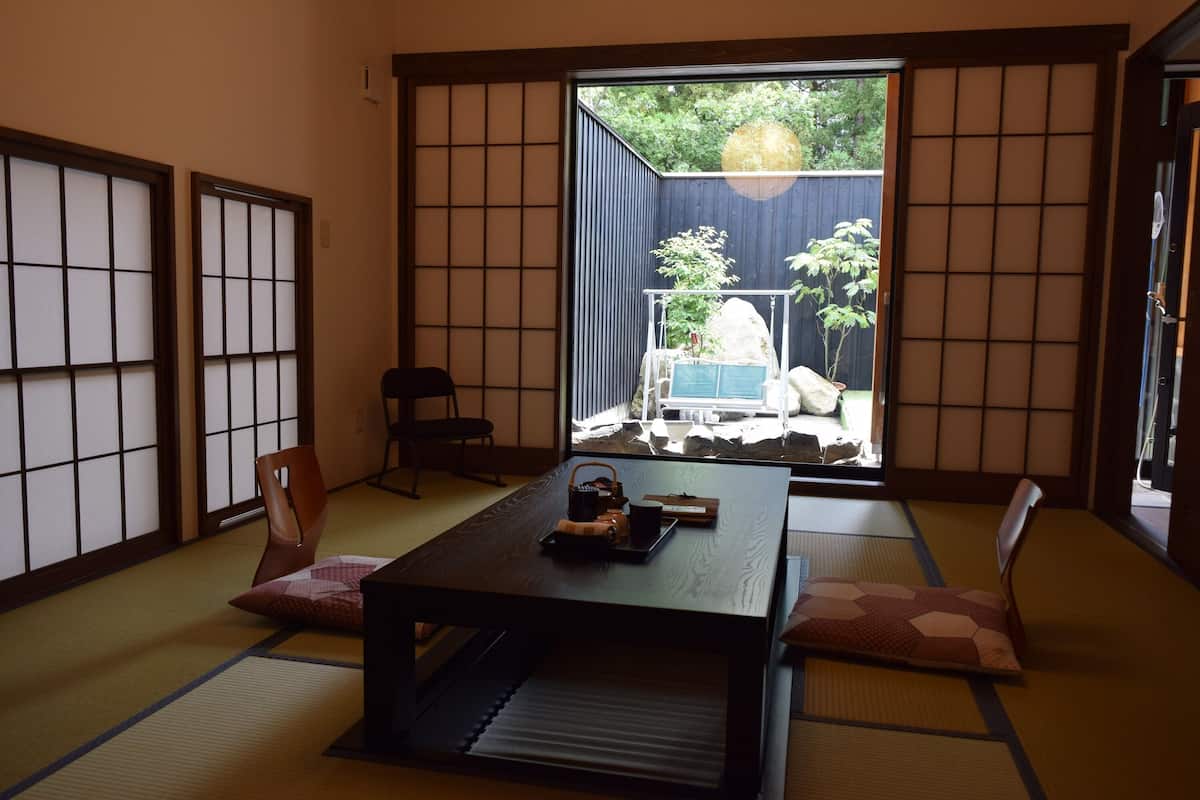 Una habitación con suelo de tatami, puerta corredera, una mesa con juego de té y vista a un jardín.