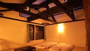 A traditional tatami mat room with a low wooden table, two tatami mats with pillows, and a window with curtains.