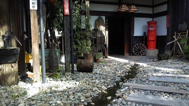 A traditional Japanese building with a stone pathway leading to a wooden door, surrounded by rocks and plants.