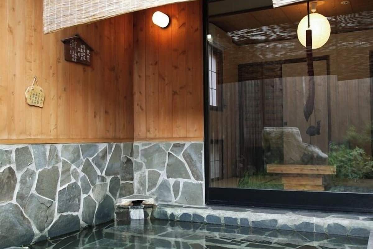 Zona de hidromasaje con baldosas de piedra, paredes de madera y puerta de cristal que da a una habitación con decoración tradicional japonesa.