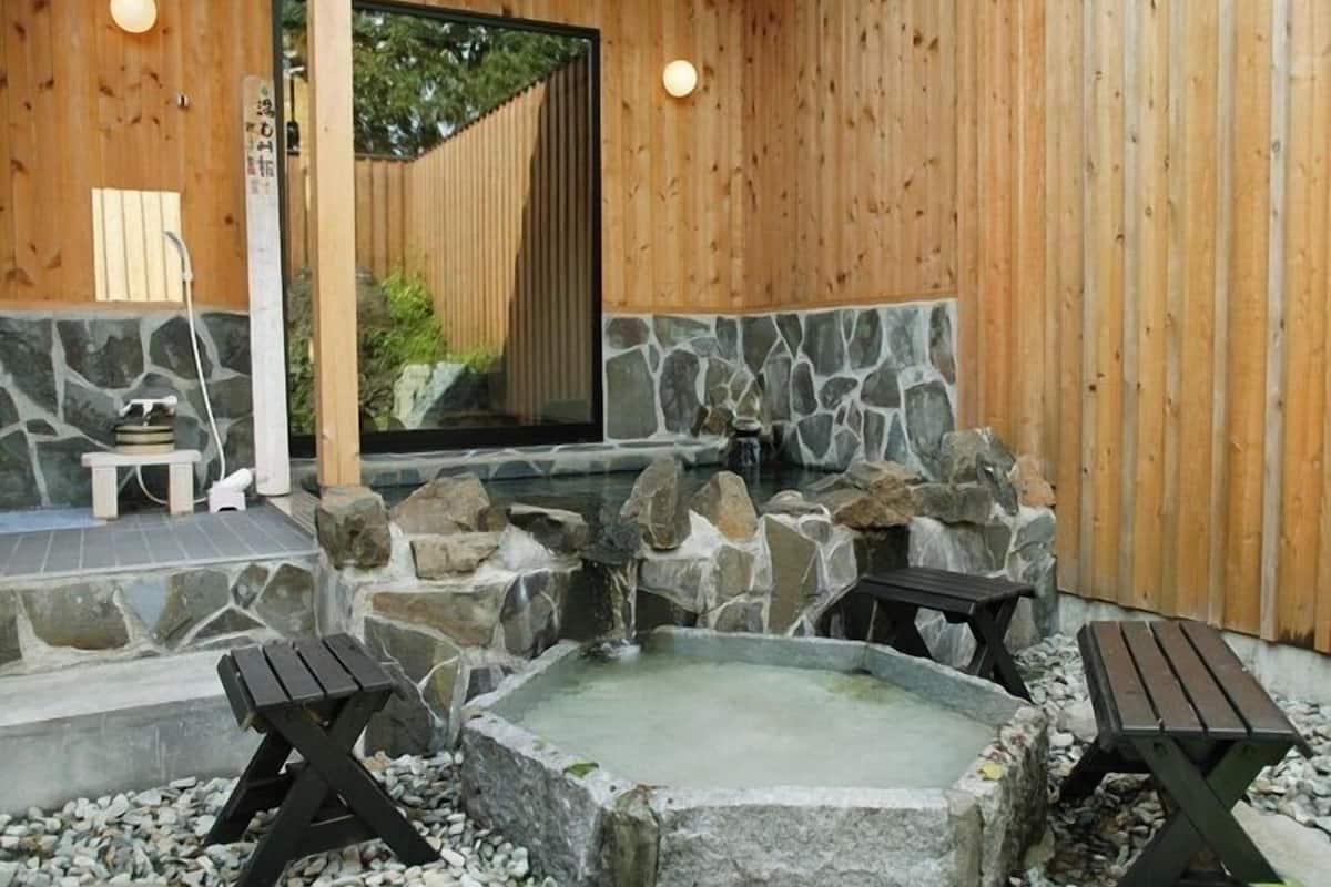 Un spa de madera con una bañera de hidromasaje de piedra, dos bancos de madera y una mesita.