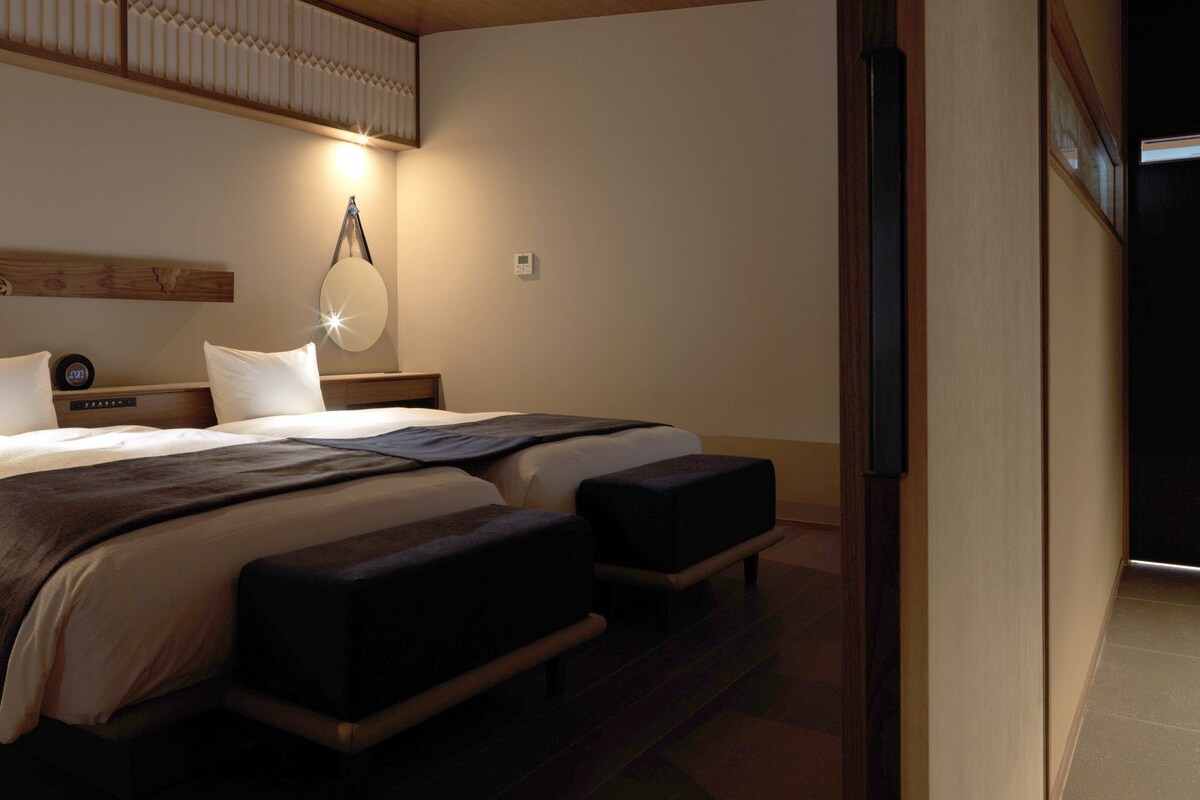 A hotel room with a large bed, bedside tables, a wall-mounted lamp, and a thermostat.