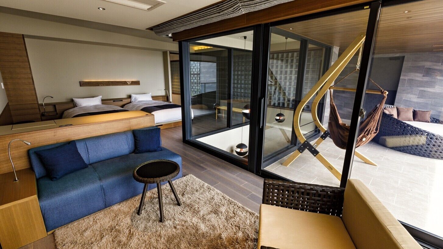 A modern hotel room with a sofa, a small round table, a glass wall, and a hammock.