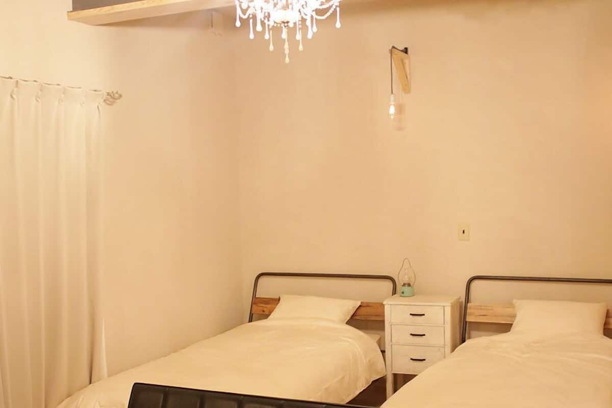 Ein Schlafzimmer mit zwei Betten, einem Nachttisch, einem Sessel und einer Deckenleuchte.
