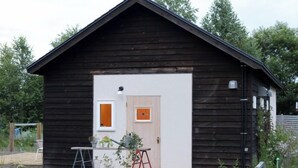 A wooden cabin with a white door, a small window, and a ladder outside.