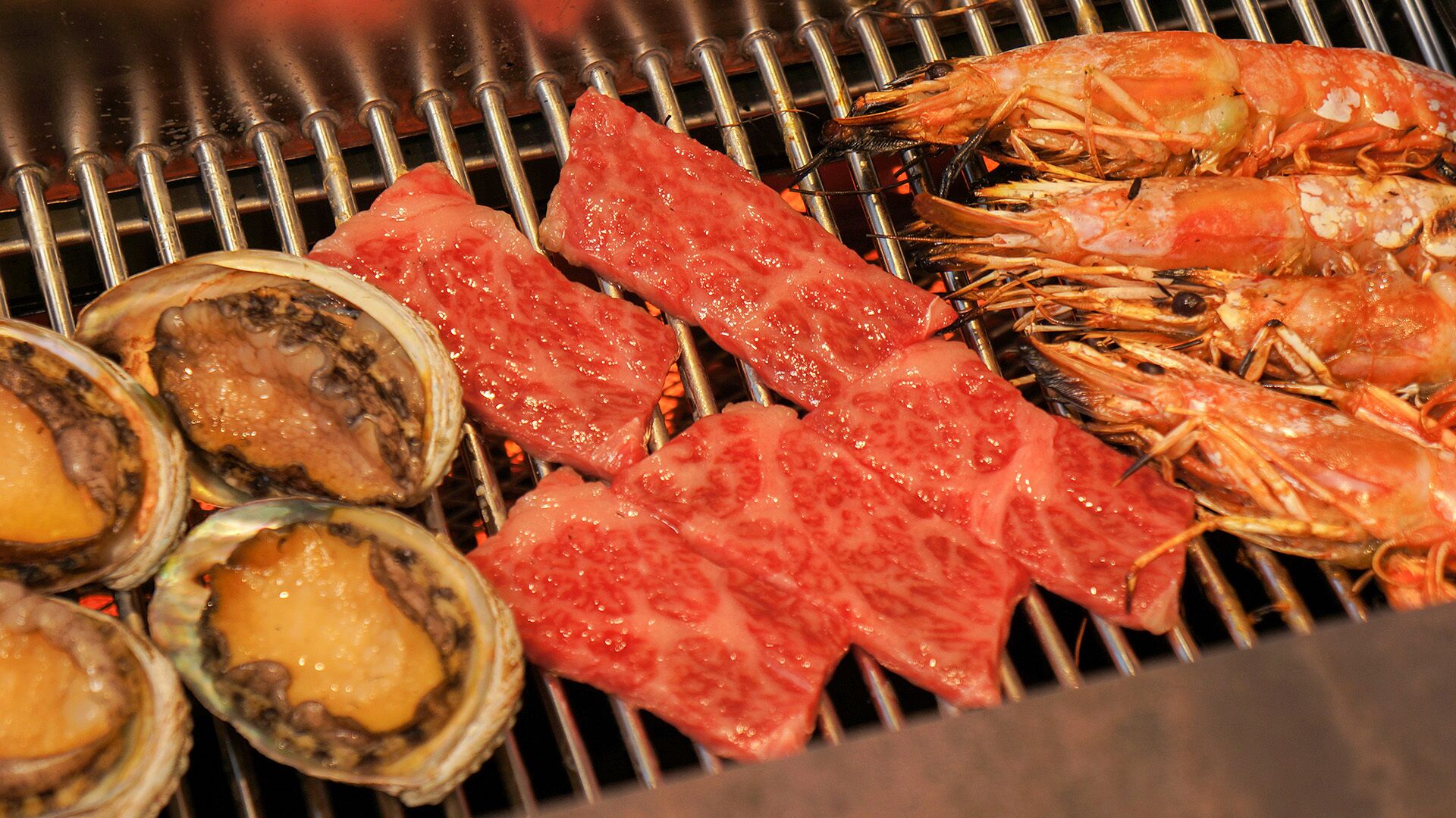 Grilled seafood including shrimp and oysters on a grill.