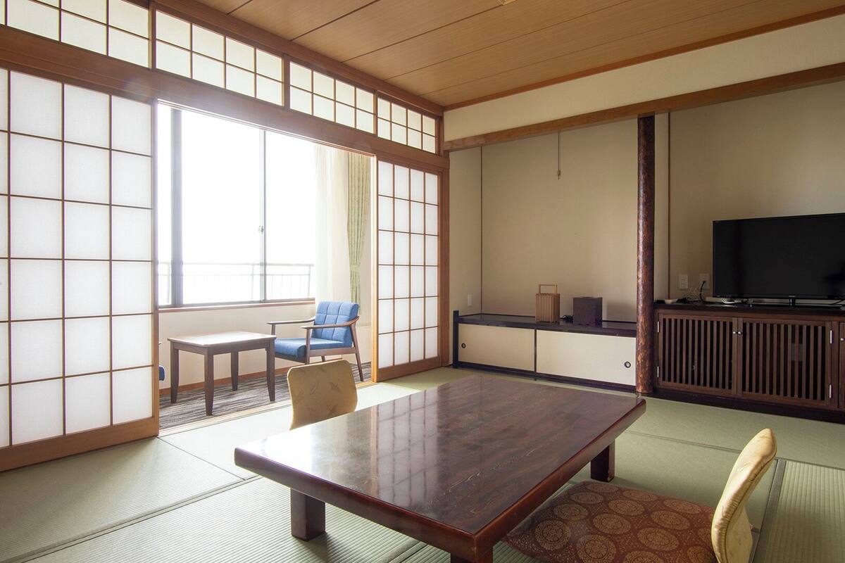 A traditional Japanese room with tatami flooring, a low table, a blue chair, a television, and sliding doors.