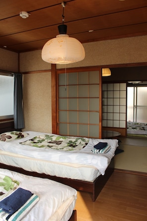 A traditional Japanese-style room with tatami flooring, a low wooden bed with a futon, and sliding shoji doors. - Jizo House (Kyoto)
