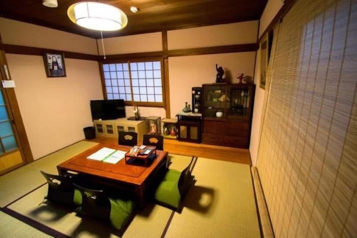 Et traditionelt japansk værelse med tatamimåtter, et lavt bord med puder, et fjernsyn og en skydedør.