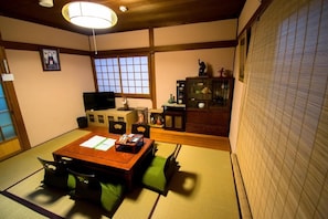 A traditional Japanese-style room with tatami flooring, a low wooden table, and a television. - Jizo House (Kyoto)