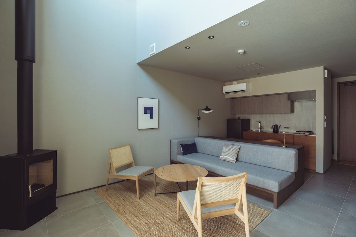 Una sala de estar moderna con un sofá, dos sillones, una mesa de centro, una chimenea y una zona de cocina.
