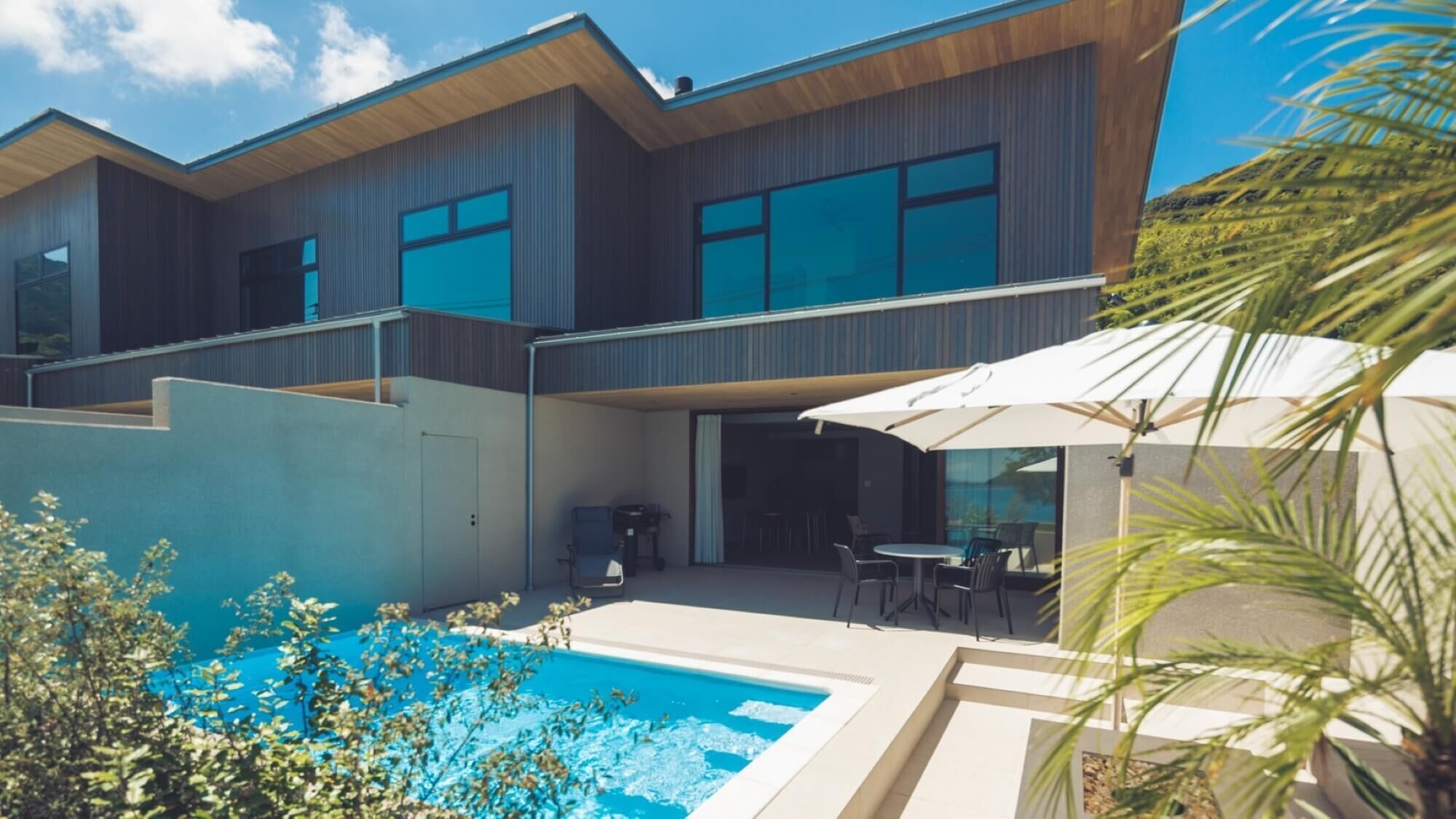 Una casa moderna de dos plantas con piscina, mobiliario exterior y un porche cubierto.