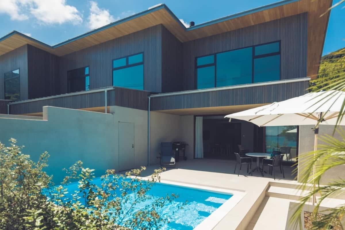 Una casa moderna de dos plantas con piscina, mobiliario exterior y un porche cubierto.