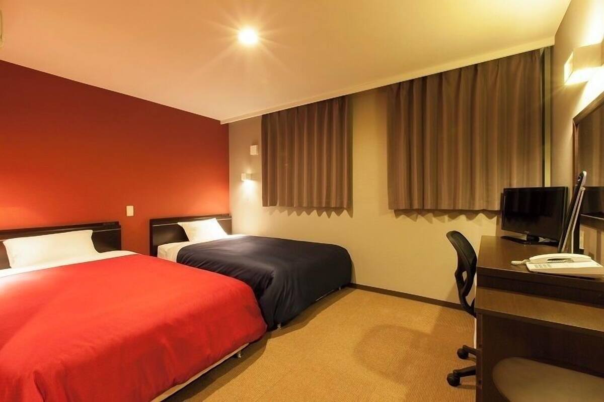 Habitación de hotel con dos camas, un escritorio, una silla, televisión y ventana con cortinas.