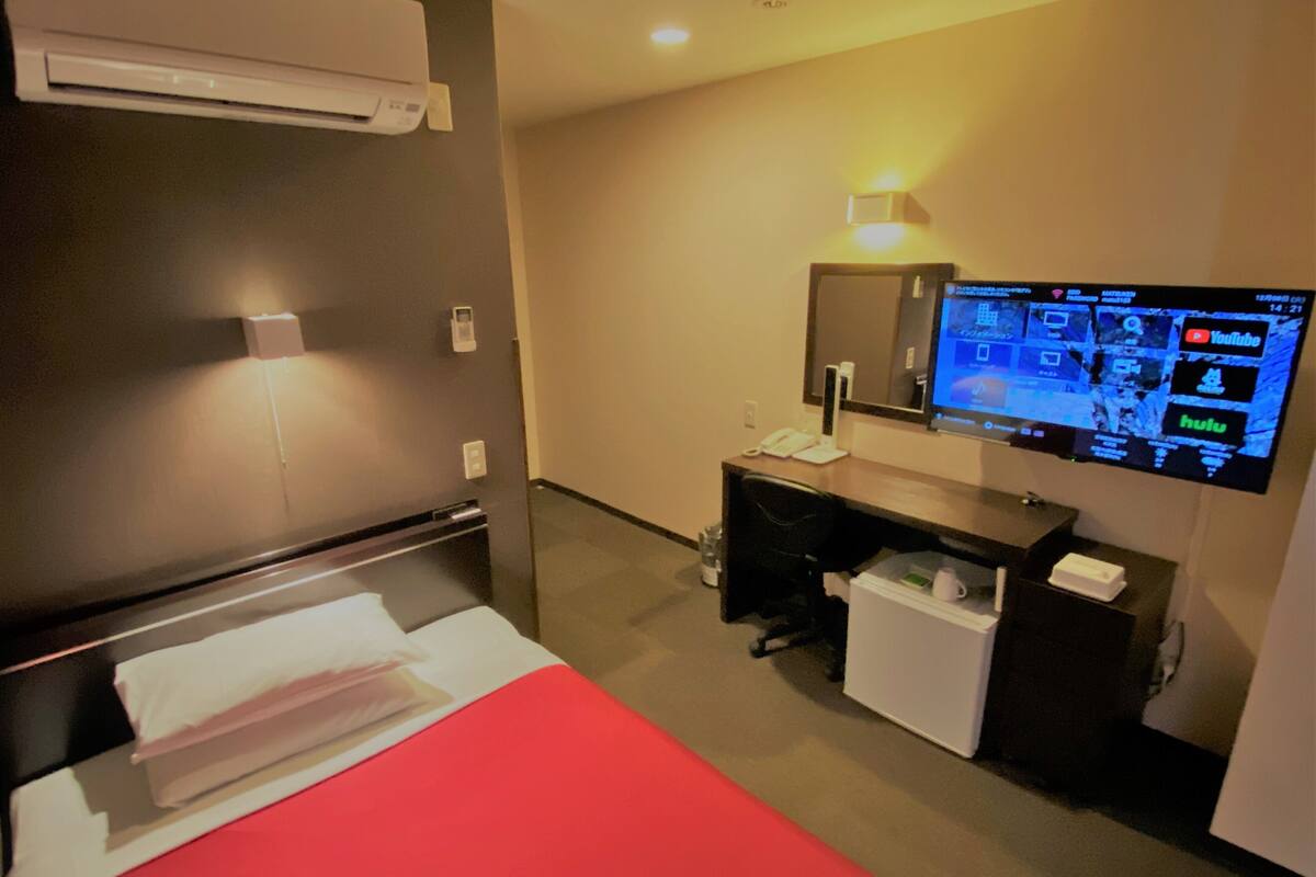 Habitación de hotel con cama, escritorio y televisor de pantalla plana montado en la pared.