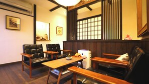 Ein traditioneller japanischer Raum mit Tatami-Bodenbelag, schwarzen Ledersesseln, einem Holztisch und einem Shoji-Bildschirm.