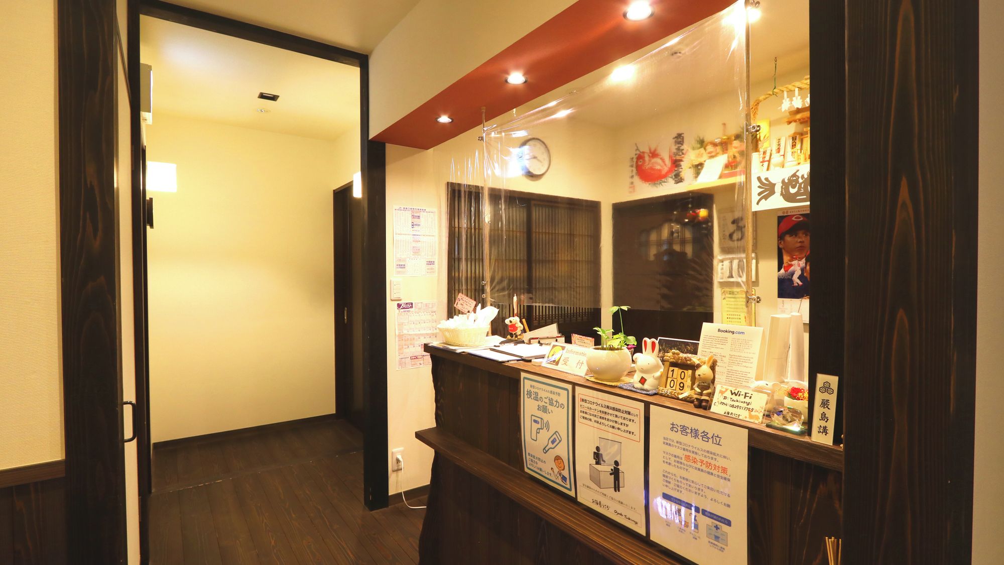 A hotel reception area with a wooden reception desk, a clock, and various informational posters.