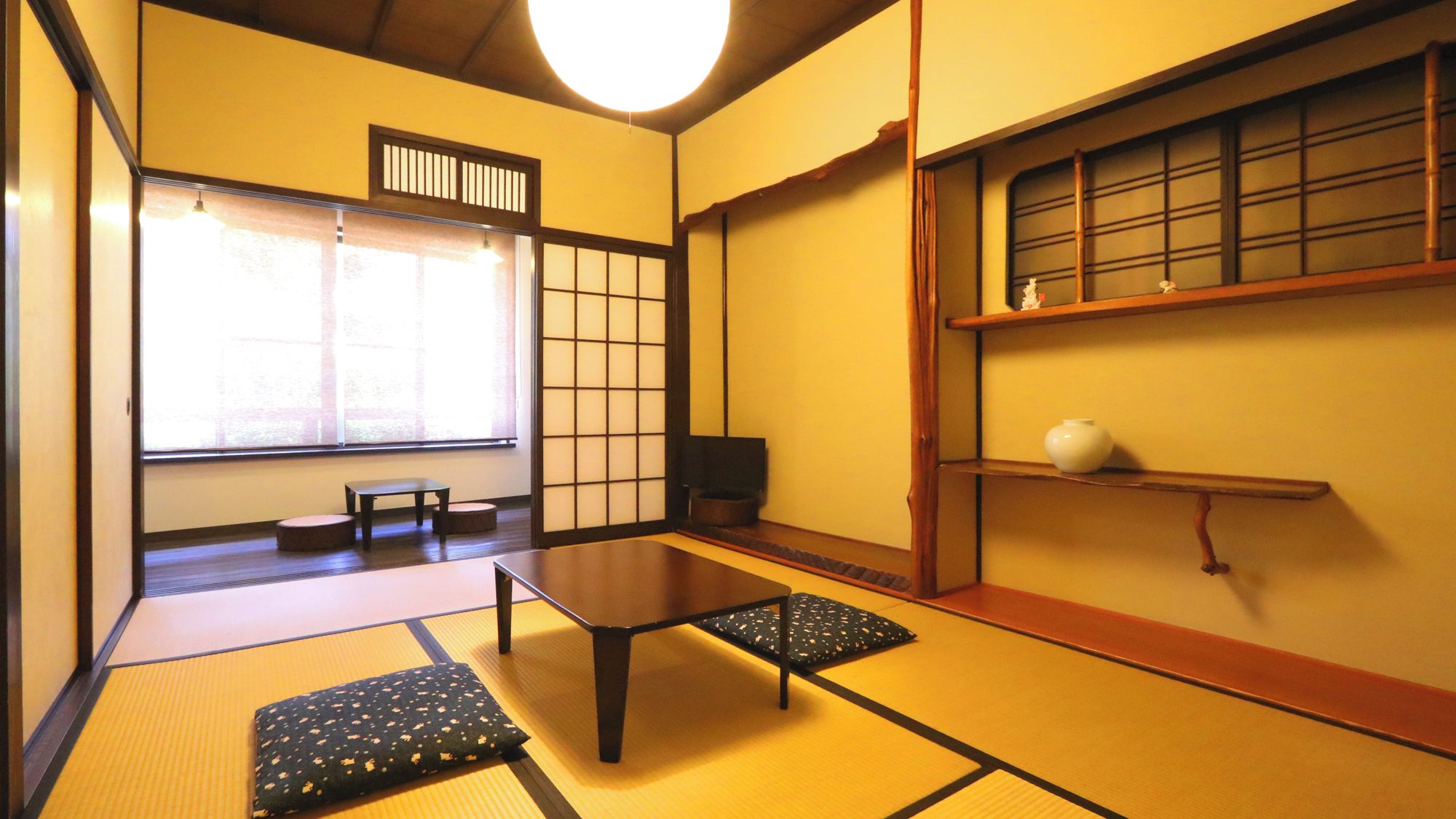 A tatami mat room with a low table, cushions, a sliding door, and a shelf with a vase.