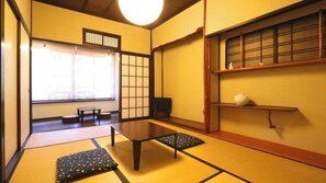 Una habitación con tatami, una mesa baja, cojines, una puerta corredera y una estantería con un jarrón.