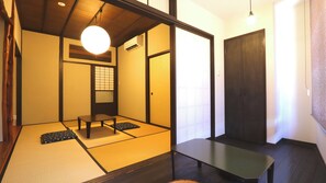 Ein traditioneller japanischer Raum mit Tatami-Bodenbelag, einer Shoji-Schiebetür, einem niedrigen Tisch und einer hängenden Leuchte.