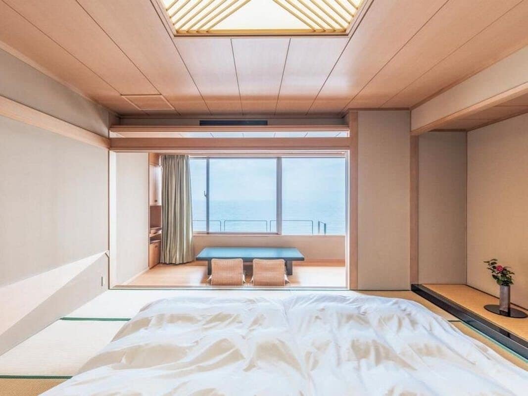 Una habitación de hotel con una cama grande, vista al mar por una ventana y un tragaluz.