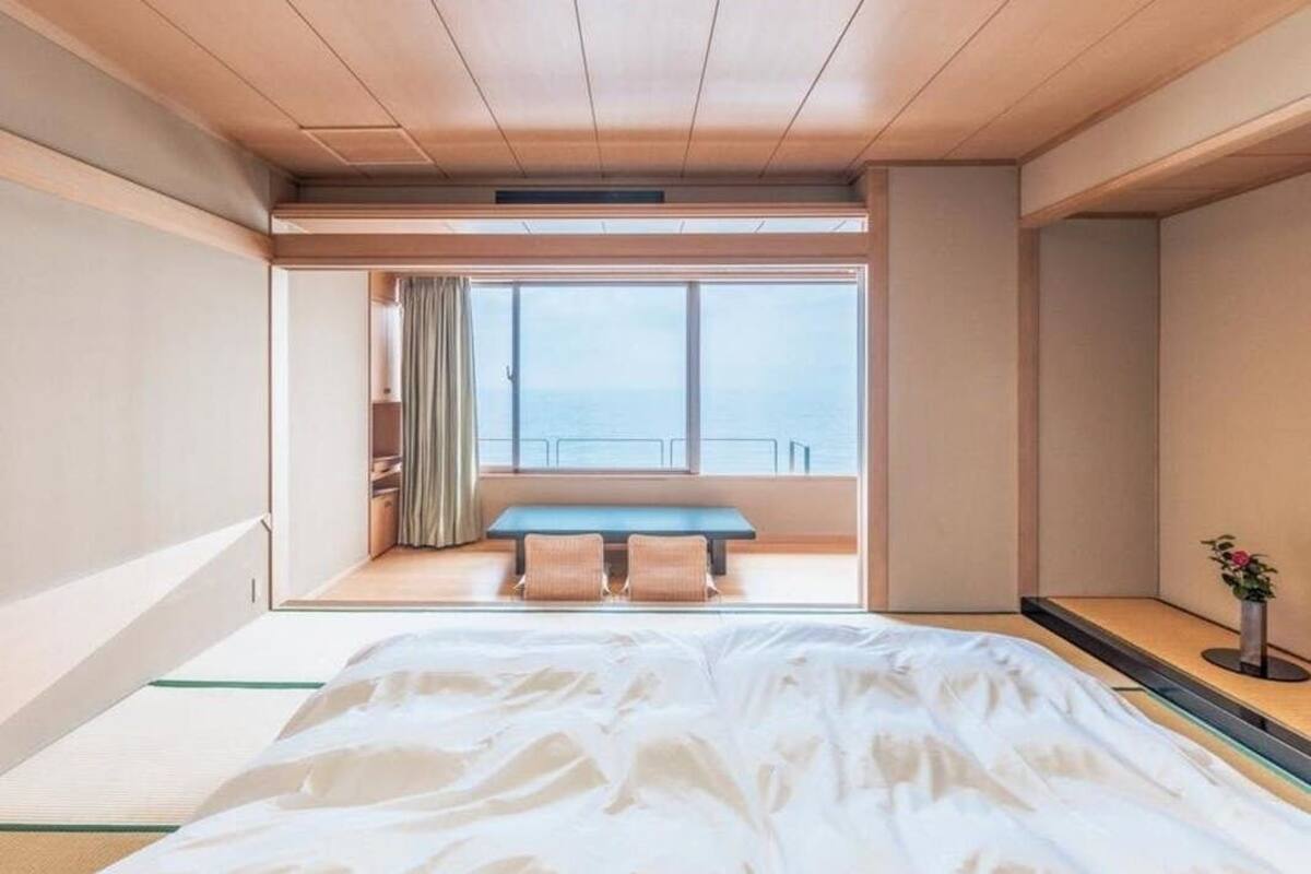 A hotel room with a large bed, a view of the sea through a window, and a skylight above.
