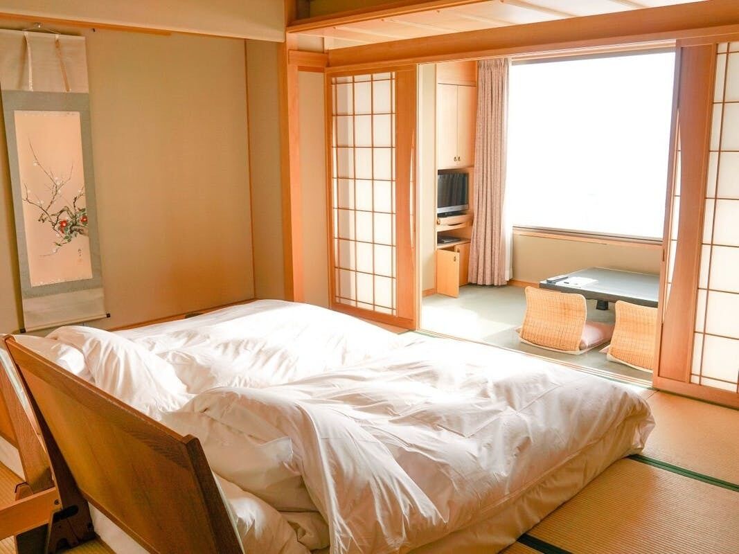 Una habitación japonesa tradicional con suelo de tatami, un futón, puertas correderas shoji y vistas a un jardín.