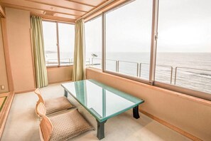 Une pièce avec une table à plateau de verre, deux chaises à motifs, une vue sur la mer par de grandes fenêtres et une balustrade de balcon.
