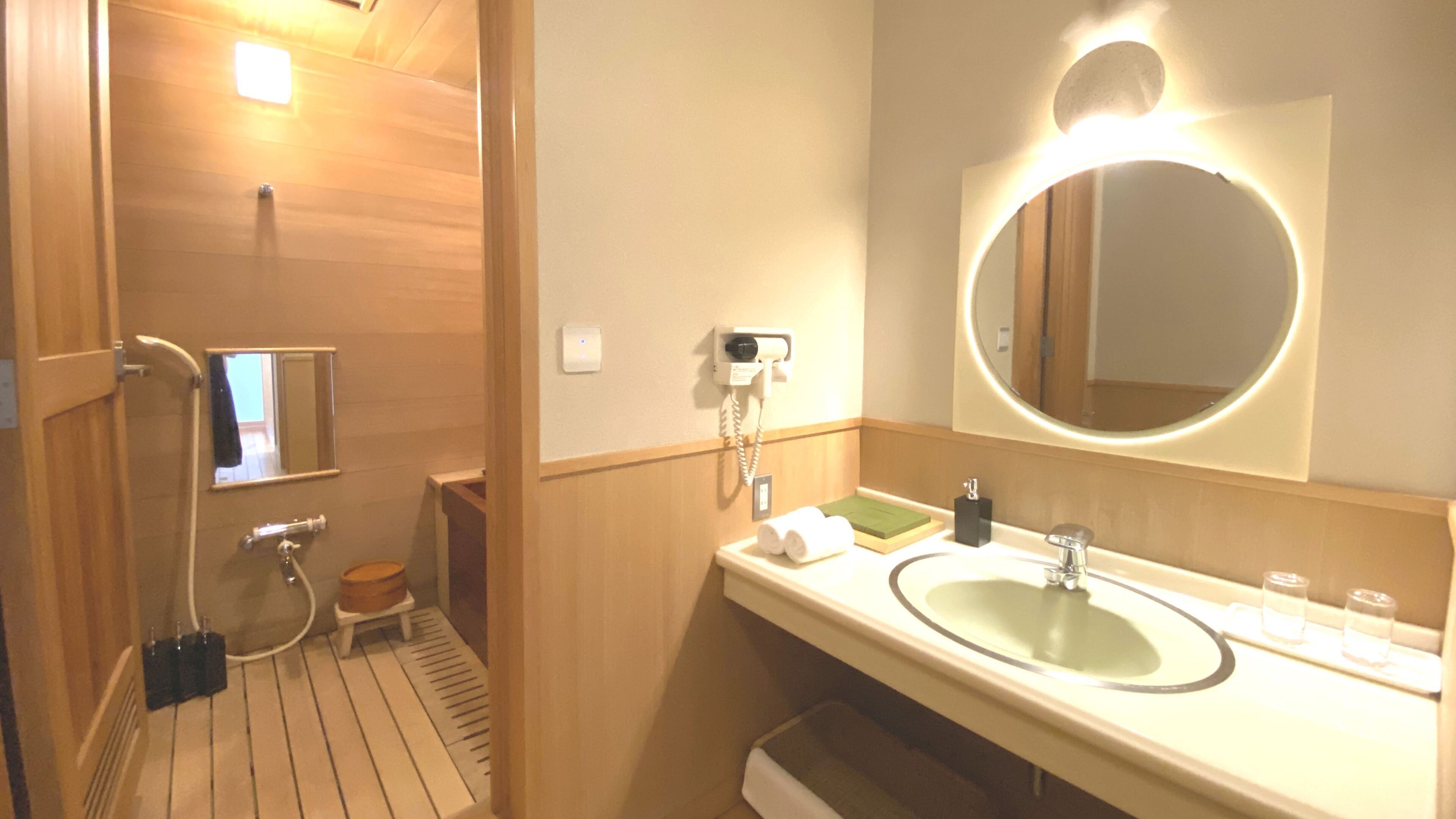 Un baño con suelo de madera, lavabo con espejo, ducha de mano e inodoro.