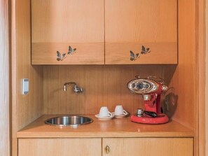 A compact kitchenette with a stainless steel sink, a red coffee maker, and two white cups on a wooden countertop.