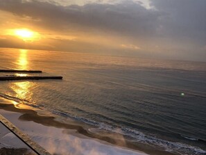 A coastal scene with a sunset over the ocean, calm waters, and a pier extending into the sea.