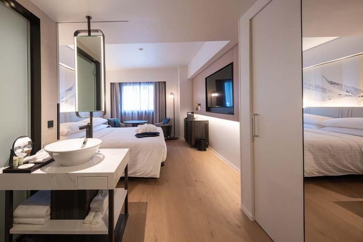 A hotel room with a large bed, a separate seating area, a desk with a mirror, and a television.