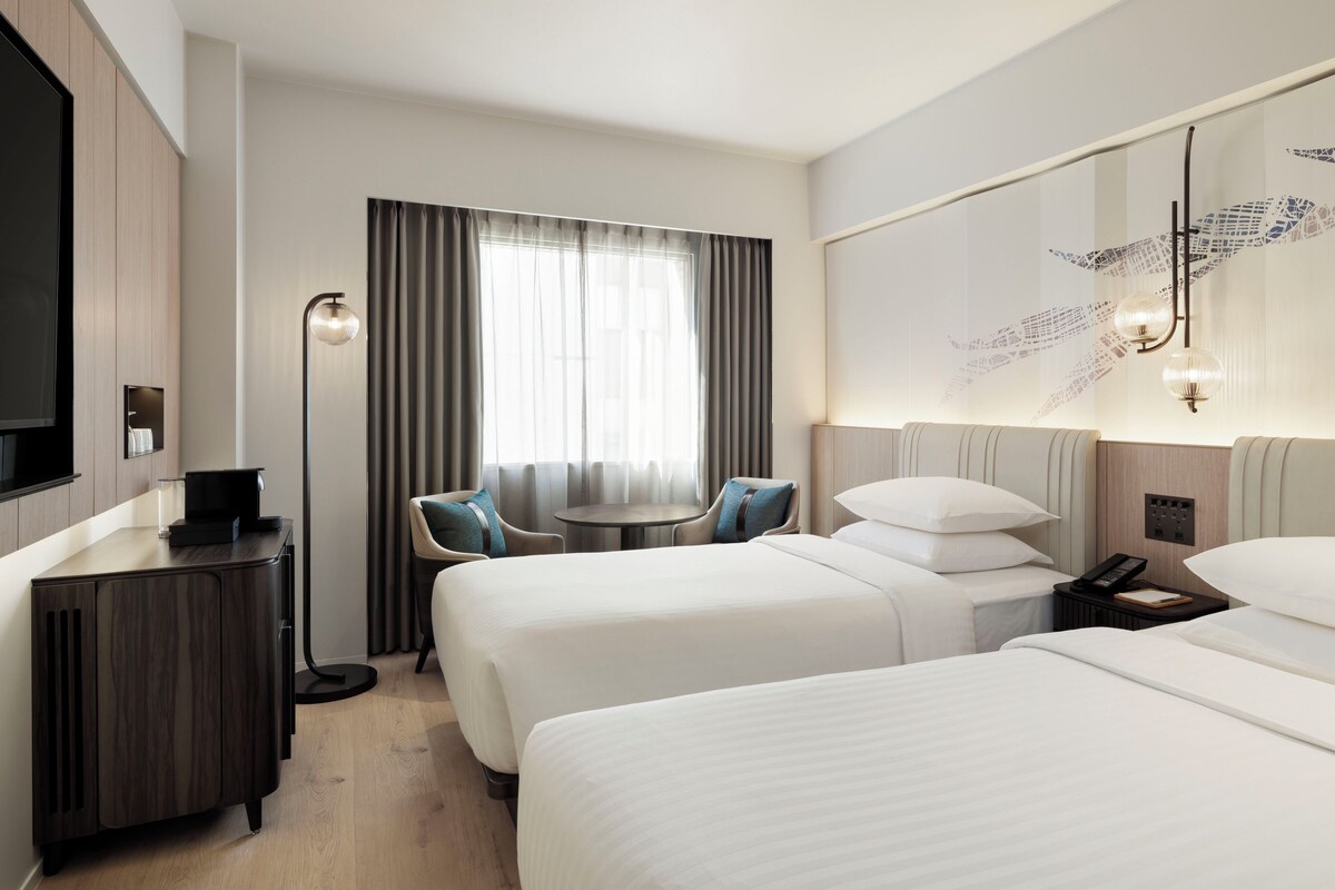 Habitación de hotel con dos camas, un escritorio con teléfono, una silla, una mesita y un televisor.