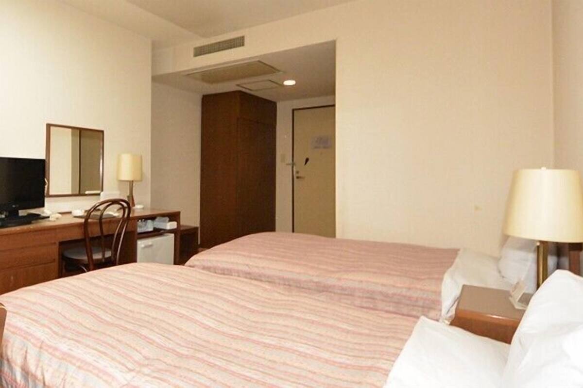 A hotel room with two beds, a desk with a chair, a television, and a lamp.