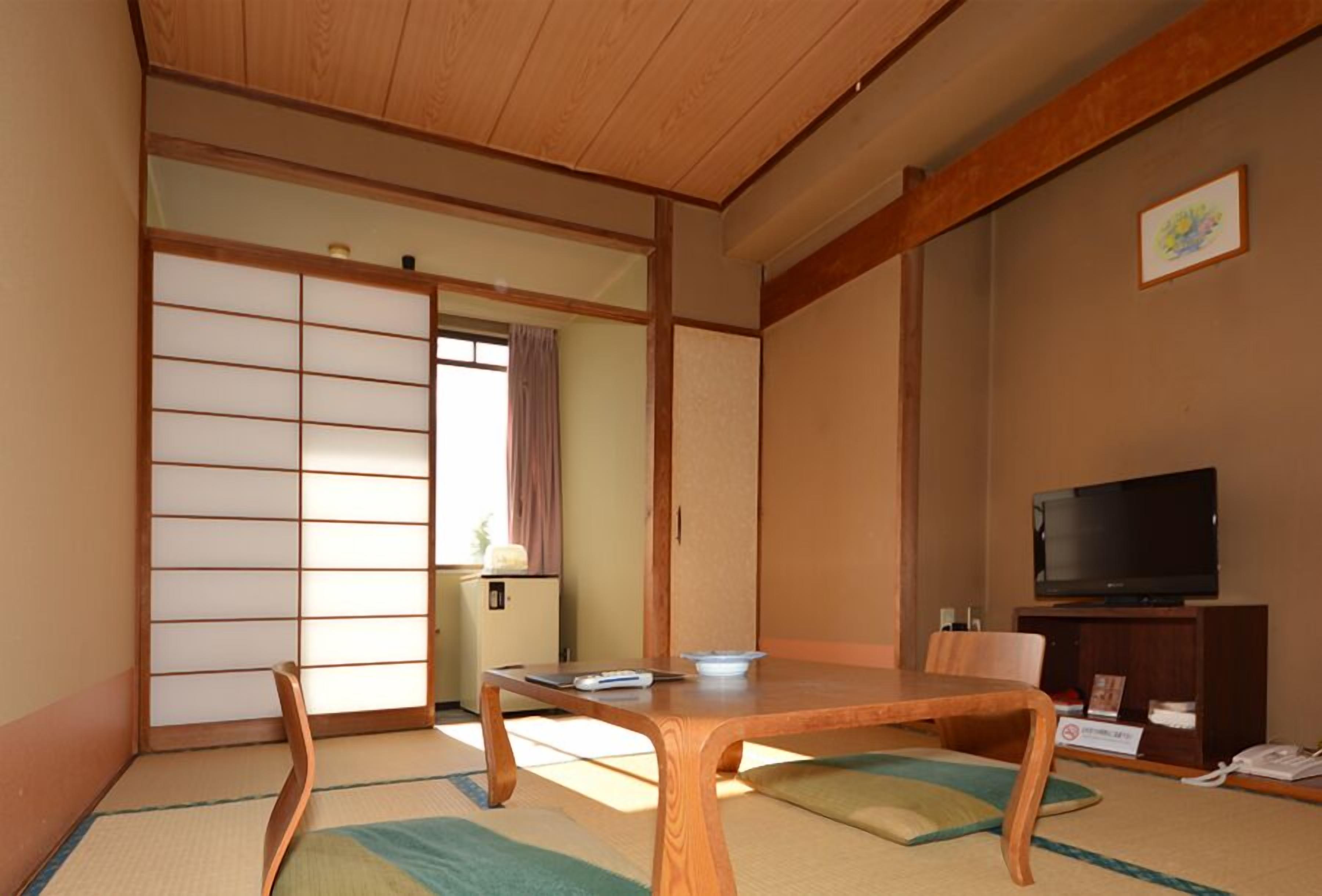 A traditional Japanese room with tatami flooring, a wooden table, a television, and sliding doors.