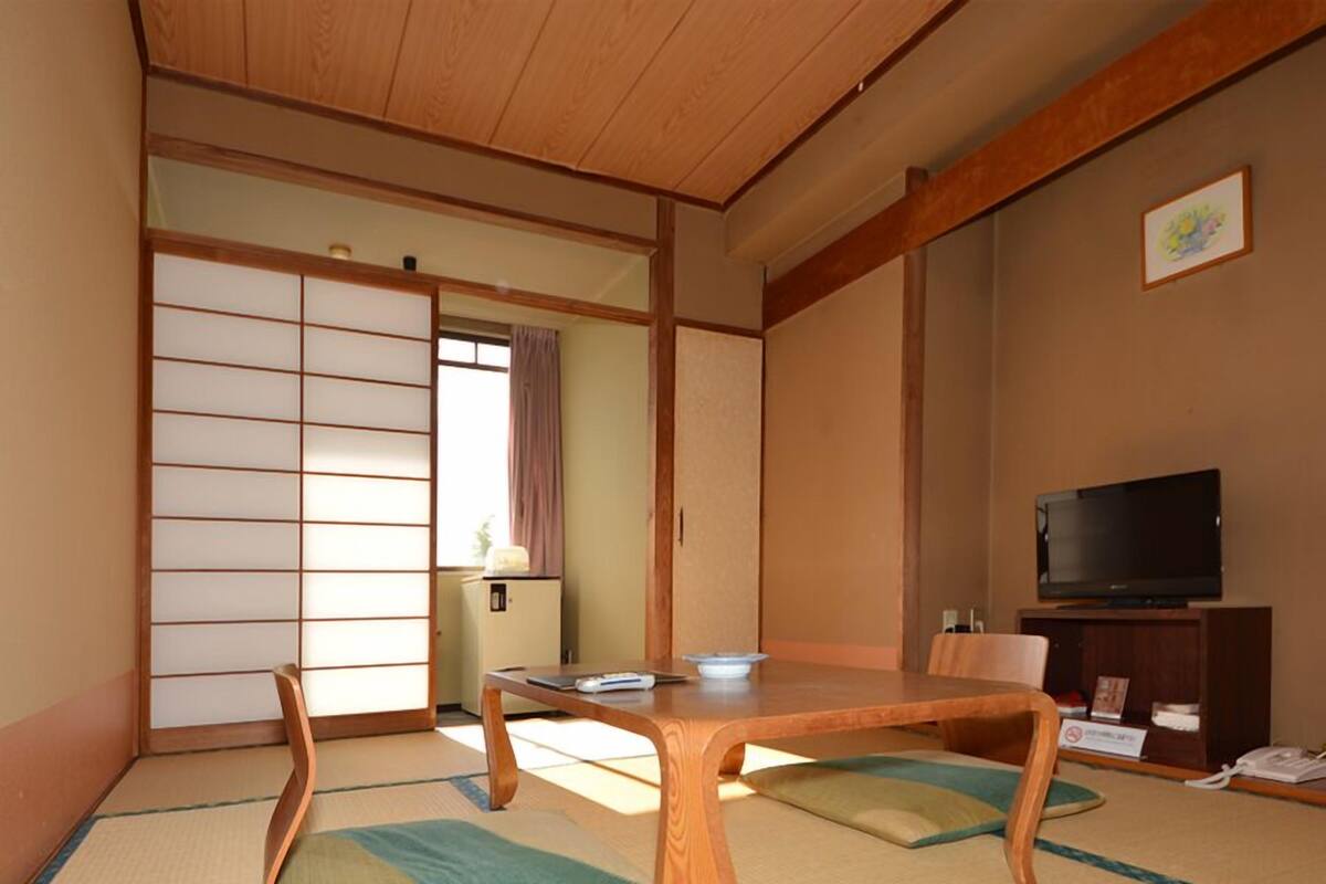 A traditional Japanese room with tatami flooring, a wooden table, a television, and sliding doors.