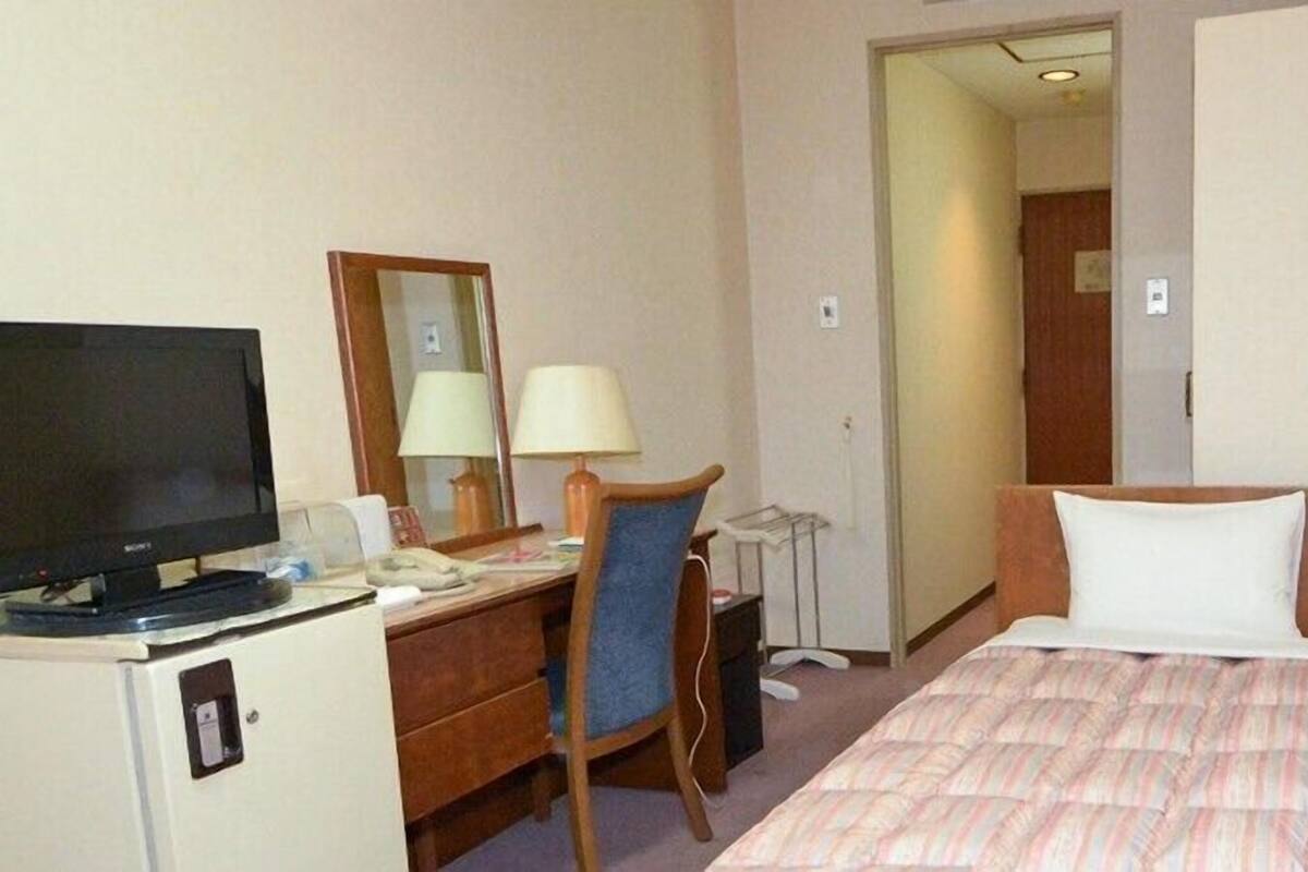 A hotel room with a bed, a desk with a computer, a television, and a mirror.