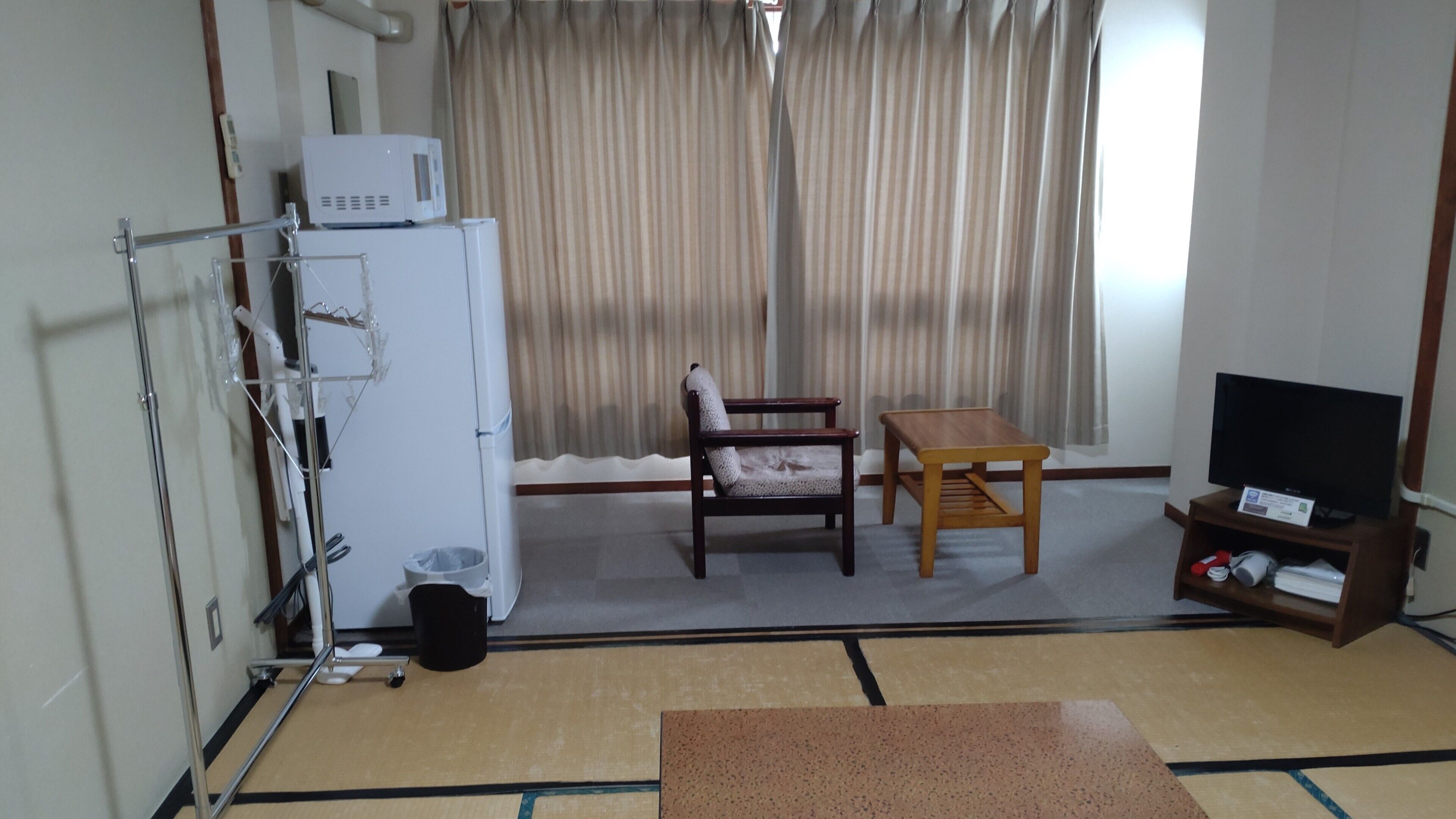 A room with a bed, a bedside table, a chair, a television, and a window with curtains.