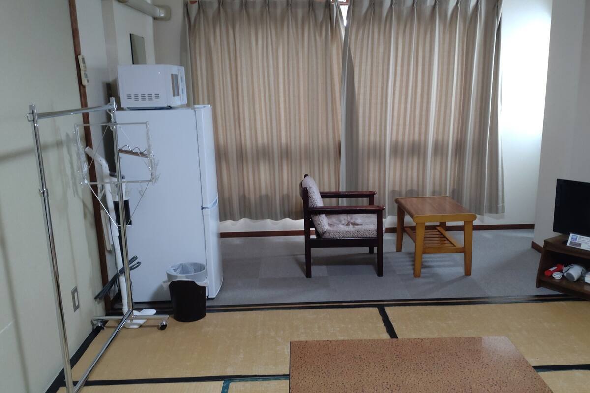 A room with a bed, a bedside table, a chair, a television, and a window with curtains.