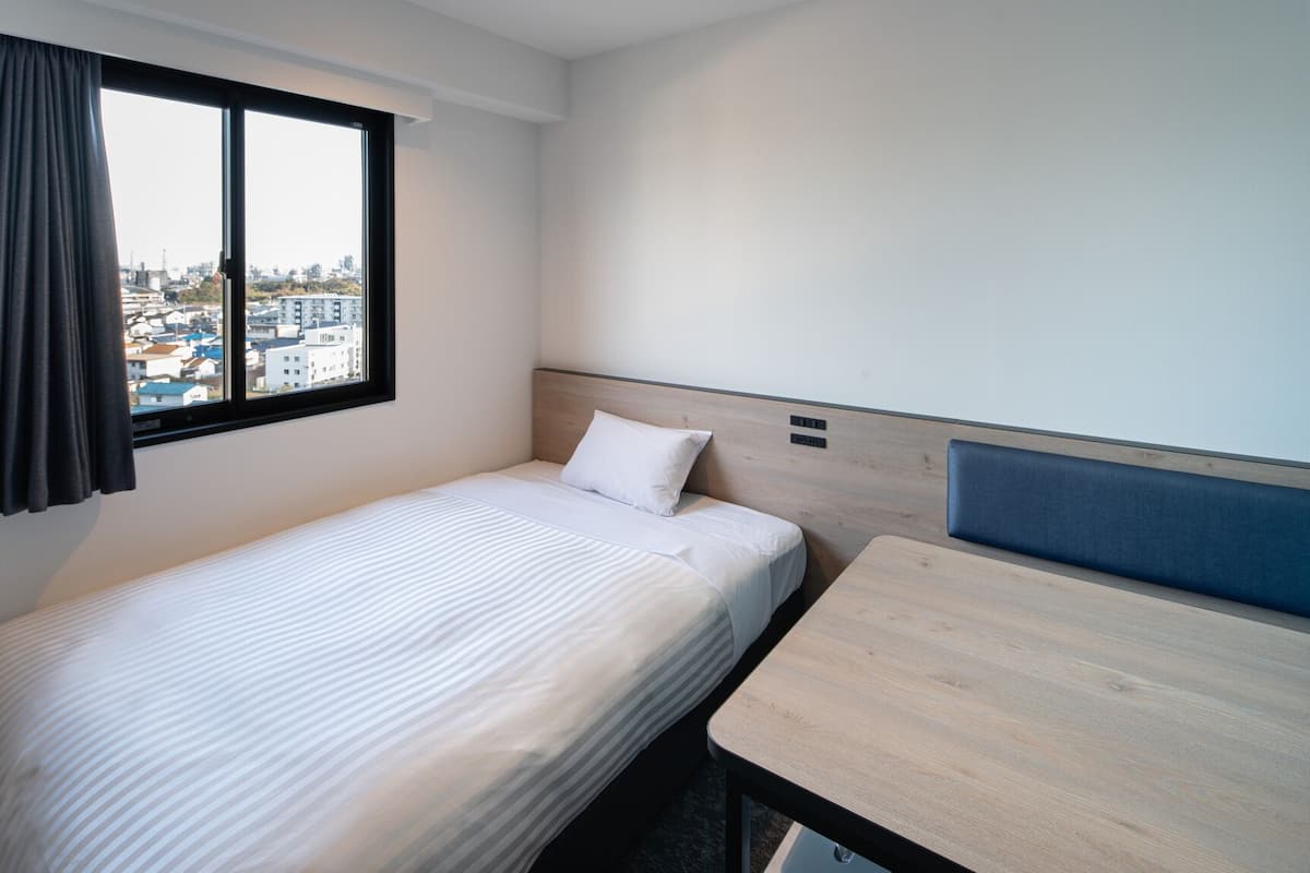 A single bed with a headboard, a small table, and a window with curtains.