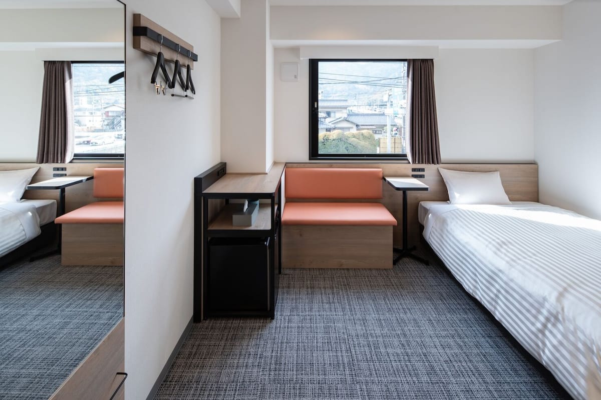 A hotel room with a bed, two seating areas, a small table, and a window with curtains.