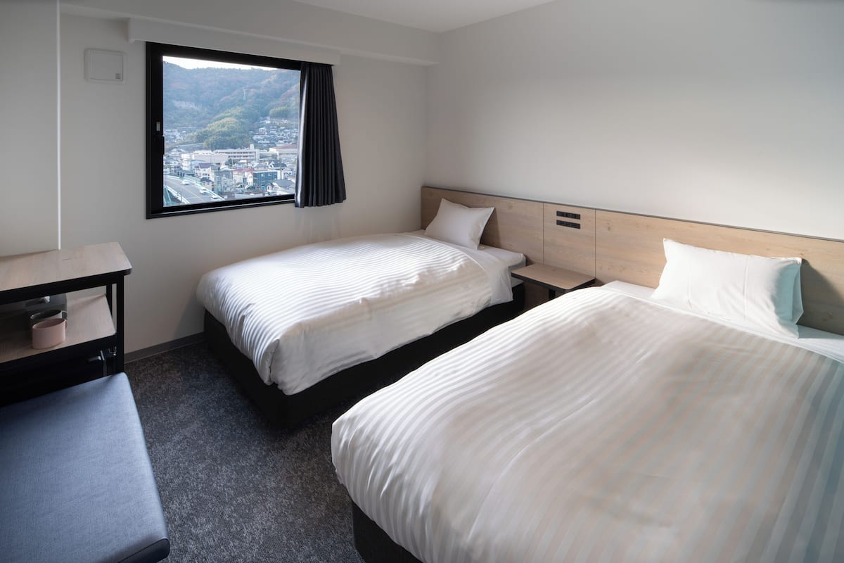 A hotel room with two beds, a desk, and a window with a view of a cityscape.