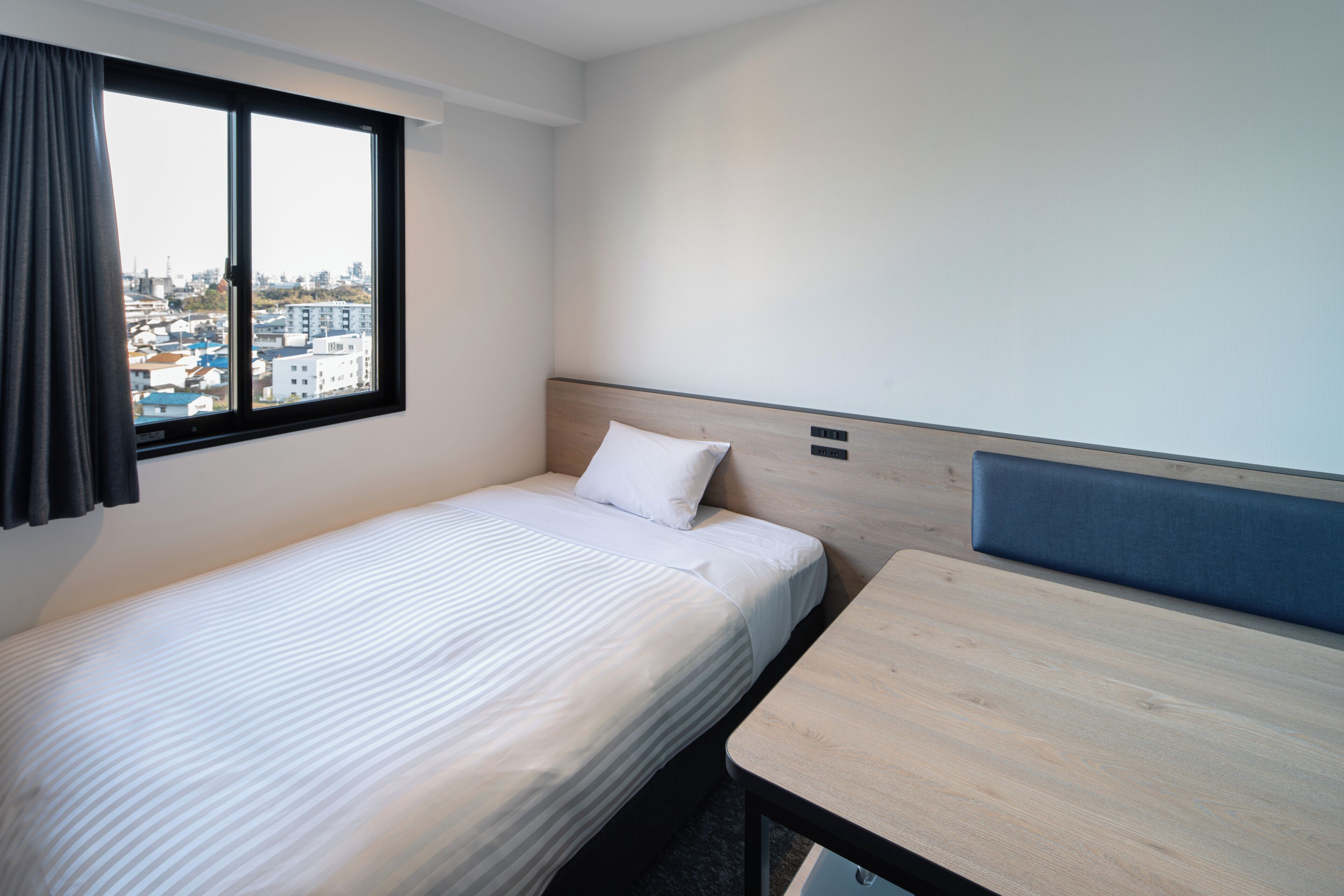 Una habitación de hotel con una cama individual, una mesita, una ventana con cortinas y vistas a la ciudad.
