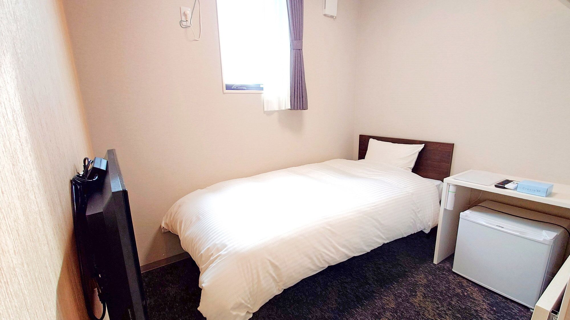 Una habitación de hotel con cama, escritorio, un pequeño refrigerador y una ventana con cortinas.