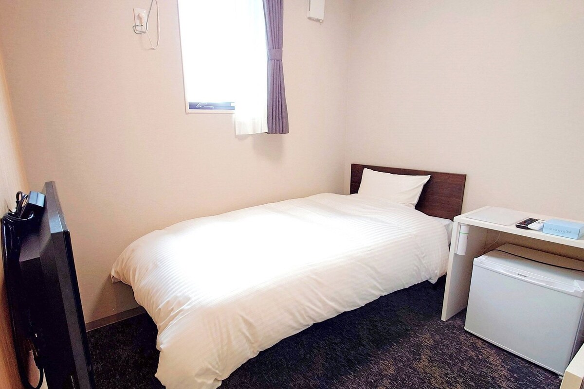 A hotel room with a bed, a desk, a small refrigerator, and a window with curtains.