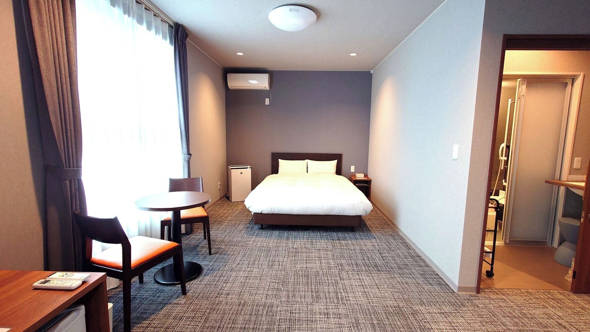 Una habitación de hotel con cama, escritorio, silla, mesita y ventana con cortinas.