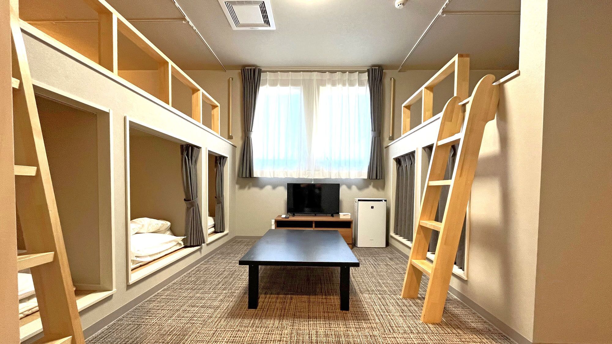 Una habitación con literas, televisión, una mesita y una ventana con cortinas.