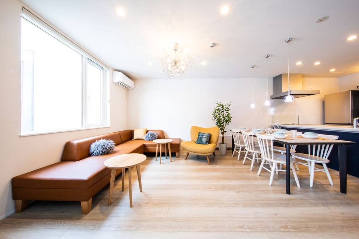 Un salon moderne avec un canapé, des tables rondes, un coin repas avec des chaises et une cuisine en arrière-plan.