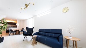 A modern living room with a blue sofa, a dining table, chairs, a potted plant, and a unique tree-shaped light fixture. - Terrace Toyohira (Sapporo)