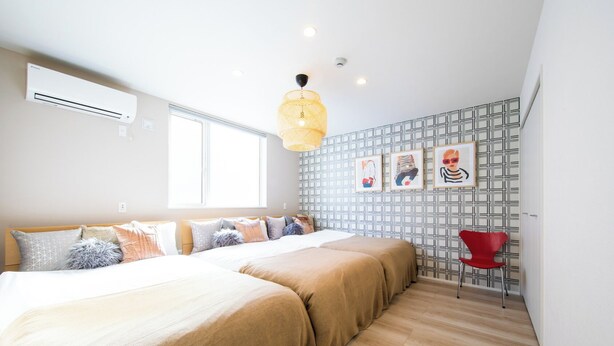 A bedroom with a bed, a window, a wall-mounted air conditioner, a hanging light fixture, and a red chair. - Terrace Toyohira (Sapporo)